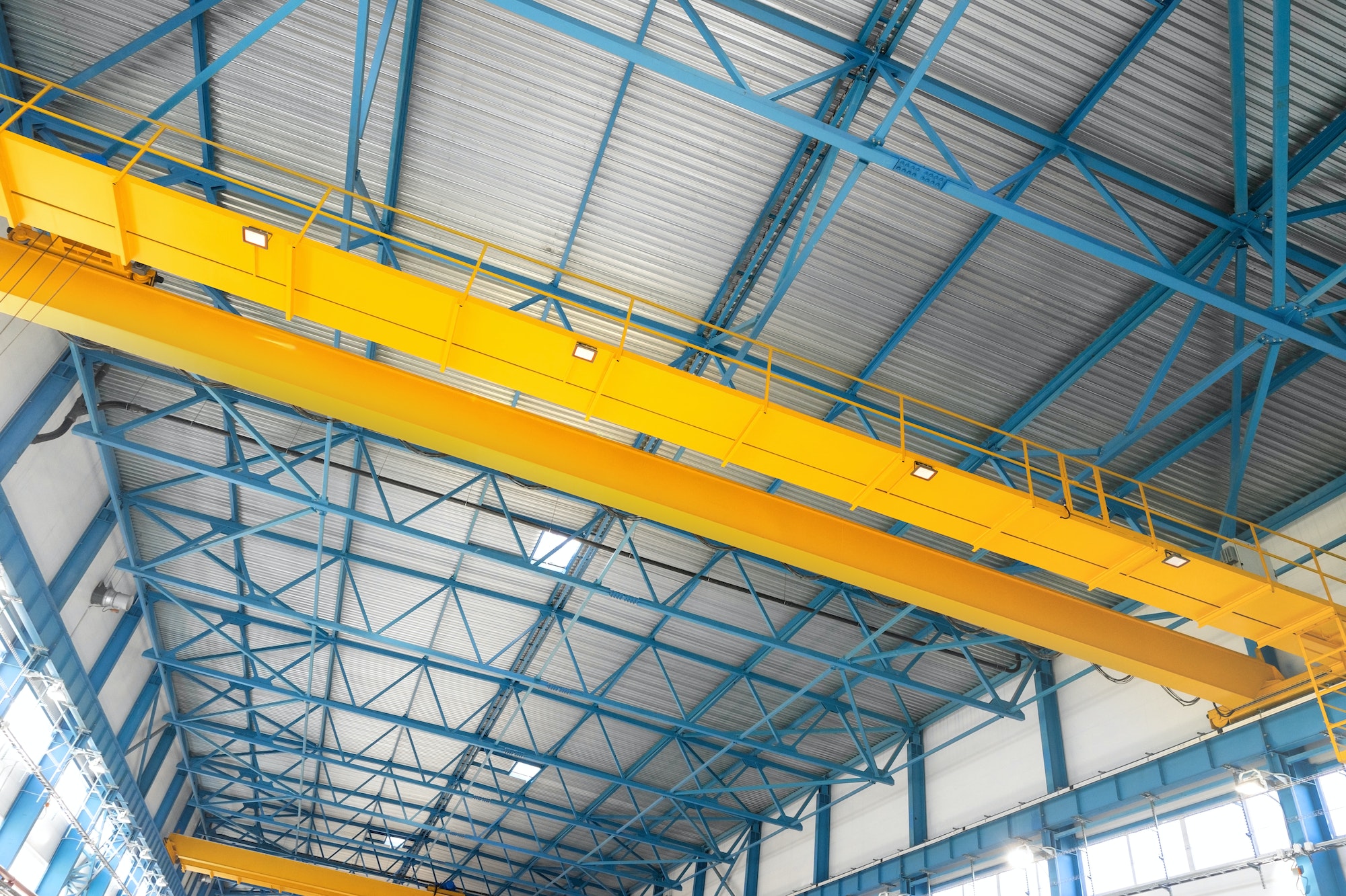 Blue steel frame of metal industrial roof in warehouse with yellow cranes under the ceiling